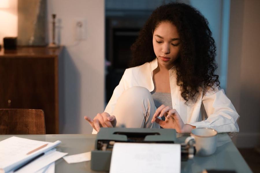 A stylish writer sits at a desk and types on an old fashioned typewriter.