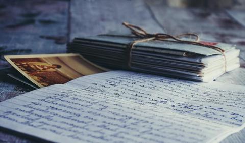 An open journal full of writing sits underneath a stack of old letters and an old photograph.