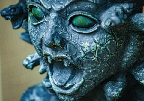 A stone sculpture of Medusa with snakes for hair, solid green eyes, and a screaming mouth.