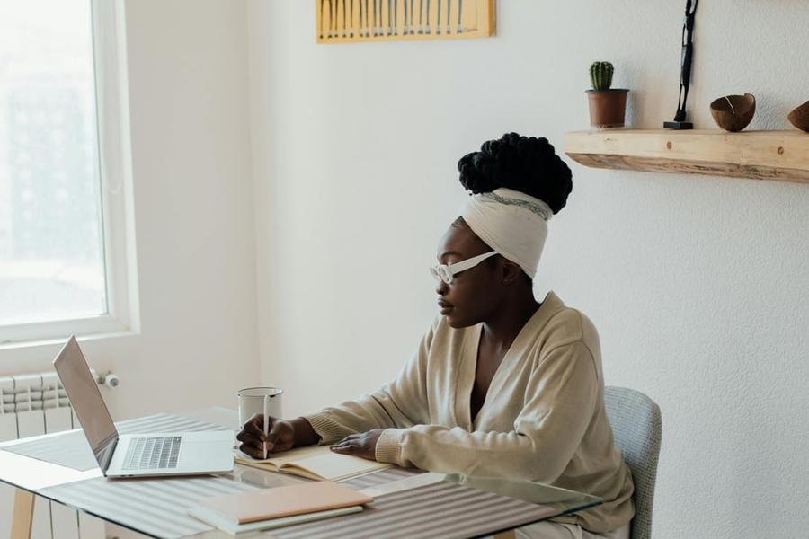 A writer with white glasses sits at a desk typing on a computer.