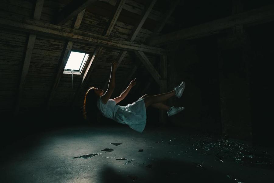 A young person wearing a dress floats in the air inside a dark, abandoned building.