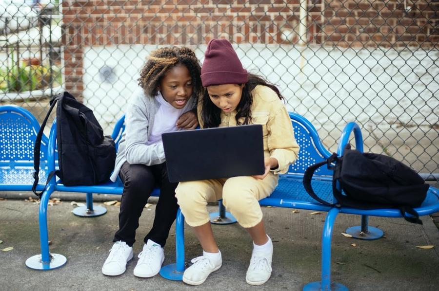 Two friends sit on a blue bench, looking intently at a computer screen.