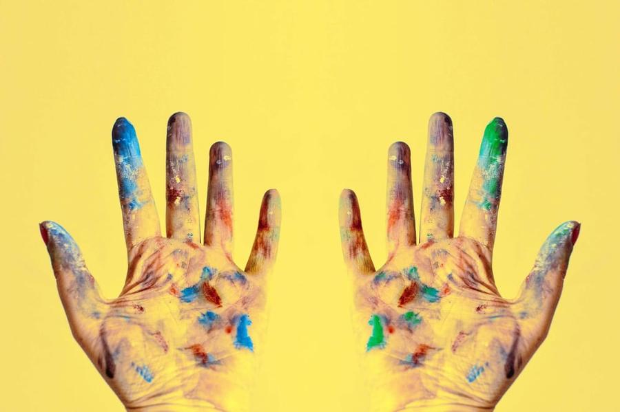 Hands covered in paint splotches over a yellow background.