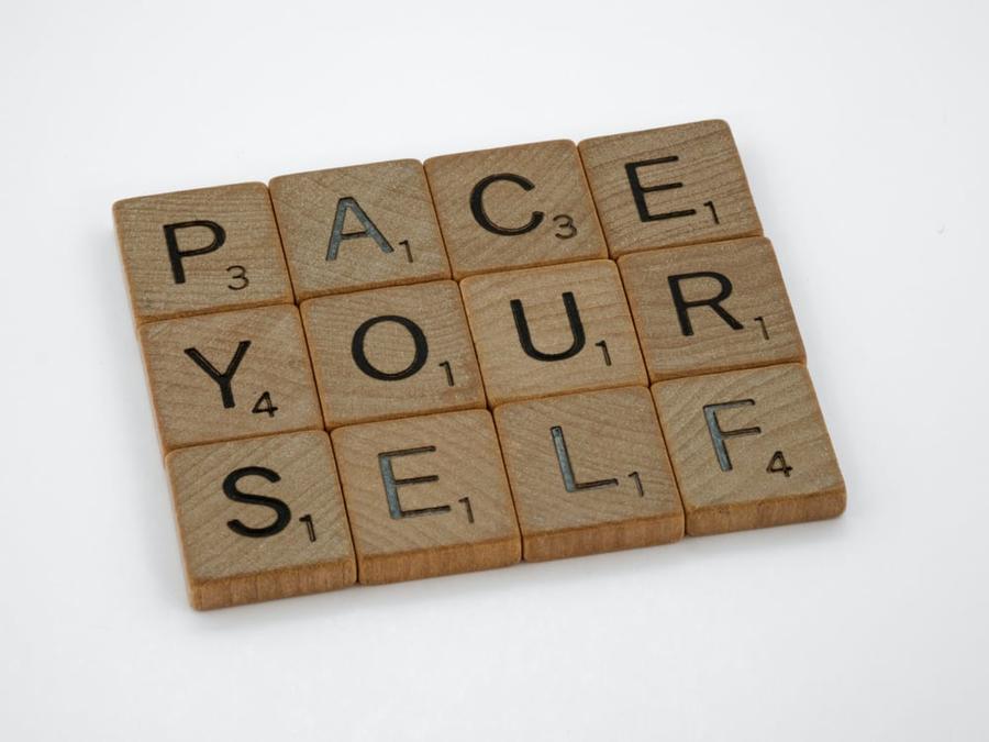 Wooden letter tiles laid out against a white background, reading "PACE YOUR SELF."