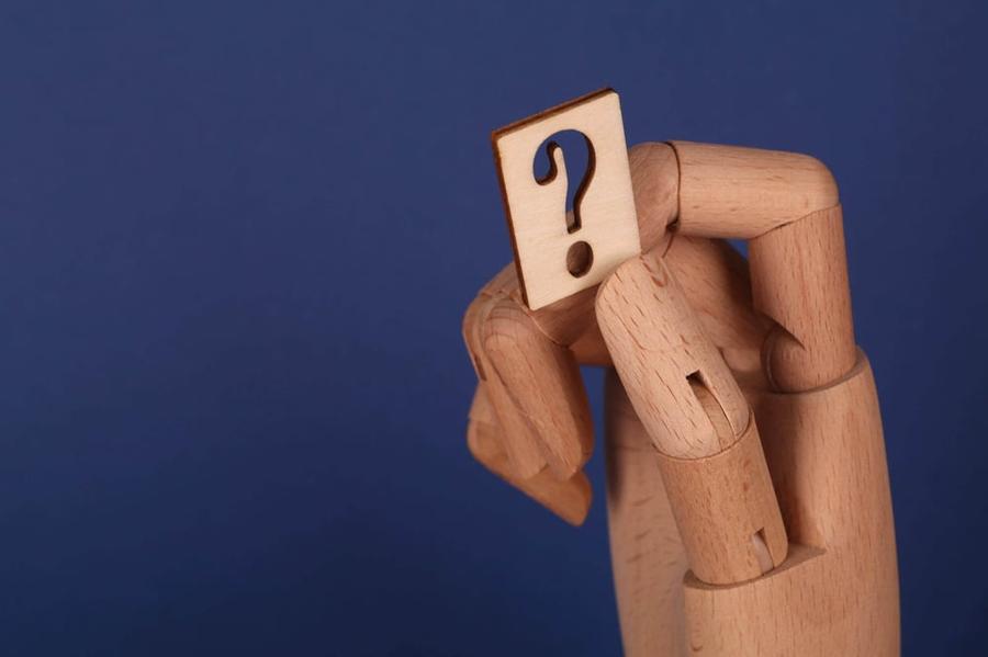 A wooden hand holds a question mark against a dark blue background.