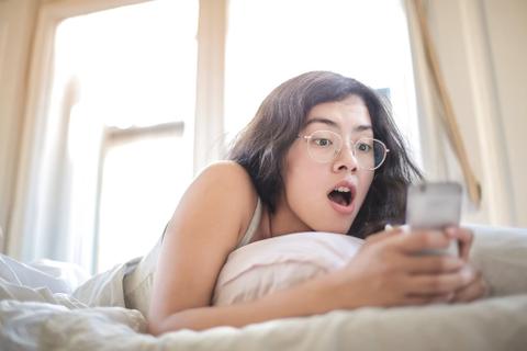 A person reads a phone in open-mouthed shock.