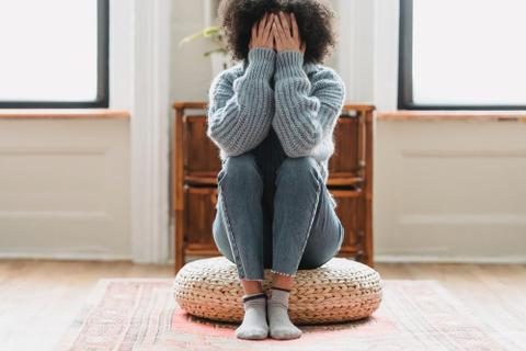 A person sits on the floor covering their face, appearing to struggle with an internal conflict.