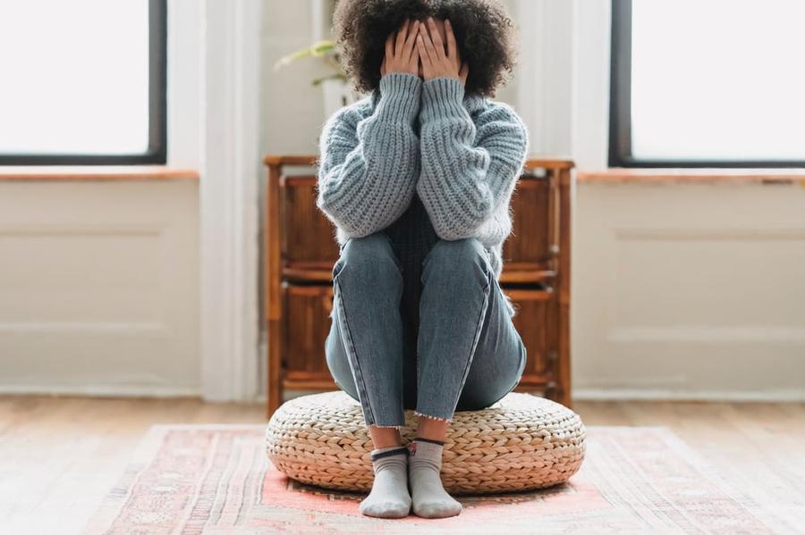 A person sits on the floor covering their face, appearing to struggle with an internal conflict.
