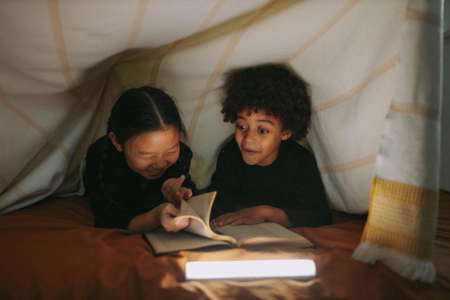 Two middle grade kids read a book together under a blanket.