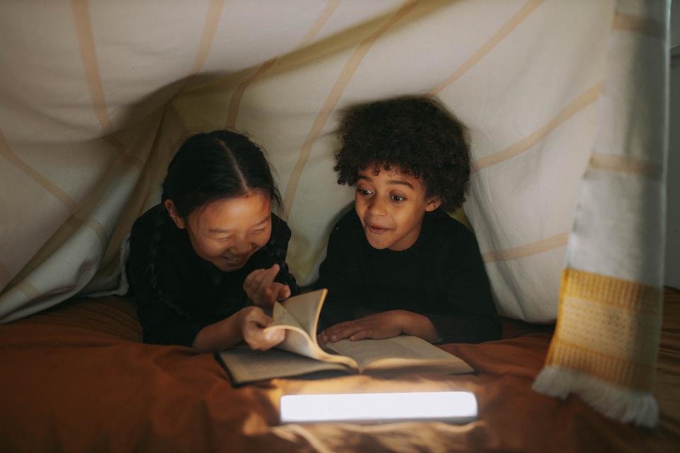 Two middle grade kids read a book together under a blanket.
