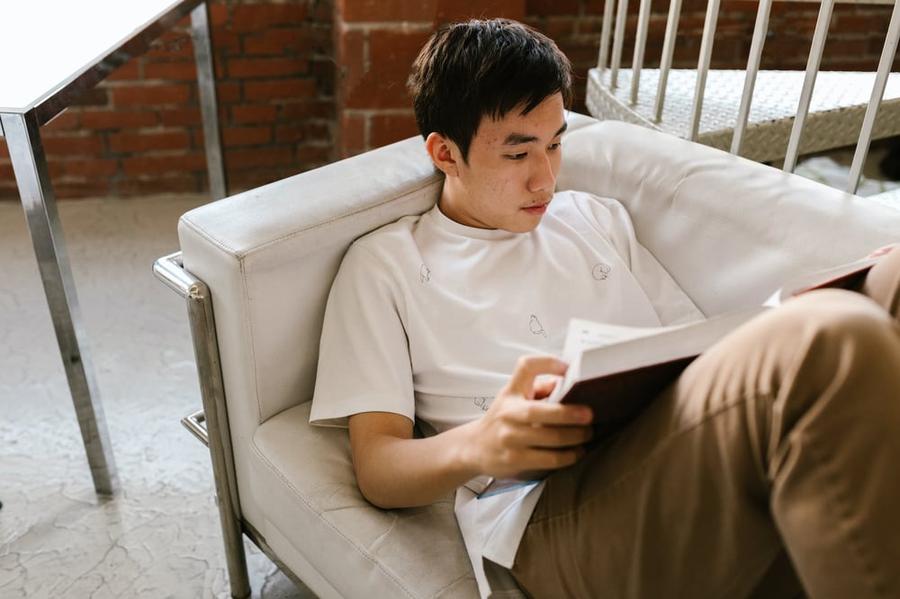 A teenager lies on a couch reading a book.