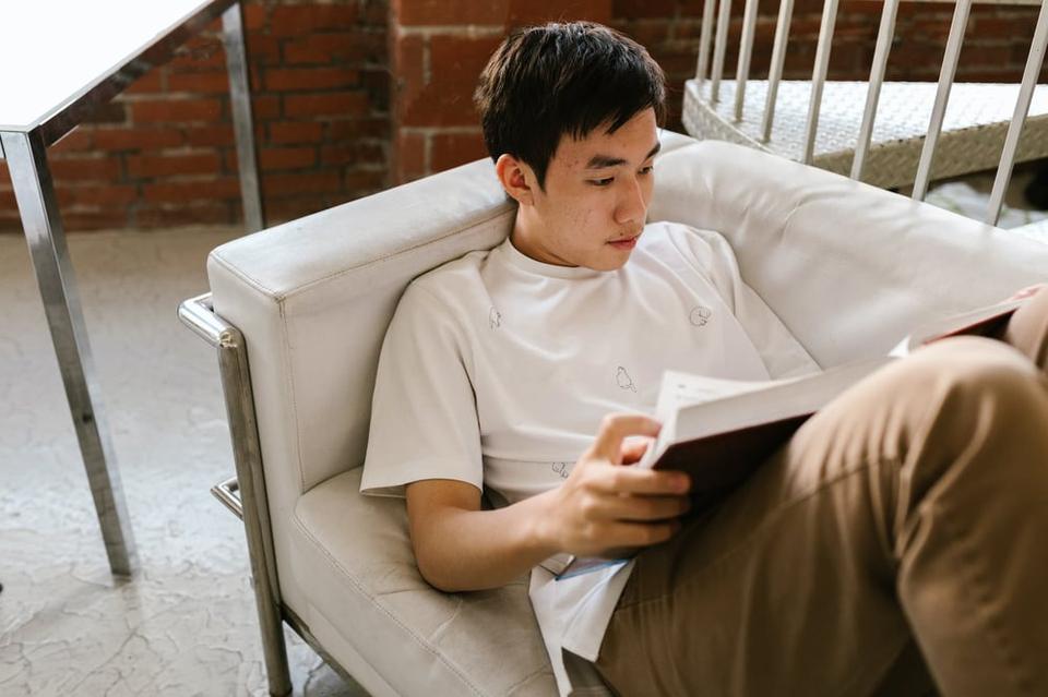 A teenager lies on a couch reading a book.