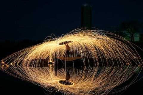 A ring of light flaring above a person with an upheld hand, their reflection in the water underneath them.