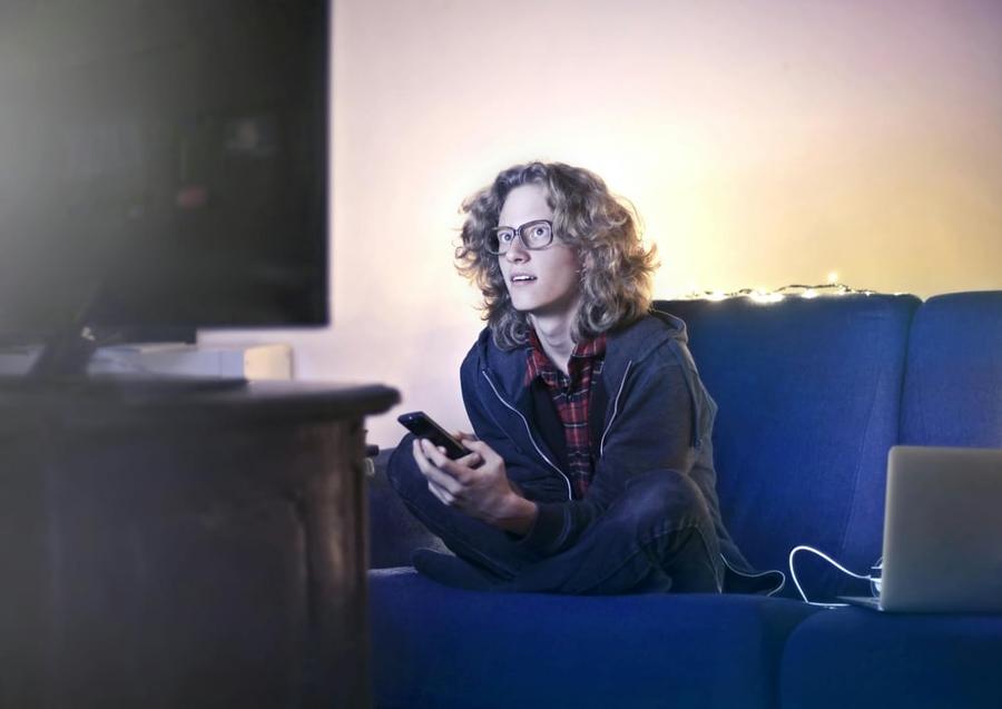 A person sits on a couch watching a movie with a hard-to-read expression on their face.