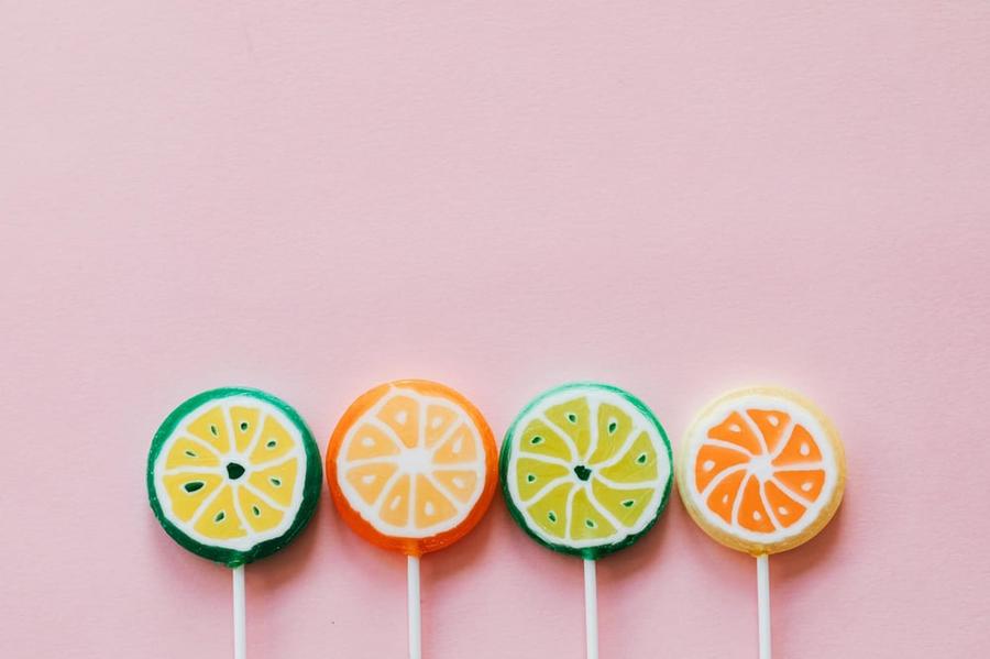 A row of four lollipops with similar designs in green, yellow, and orange.