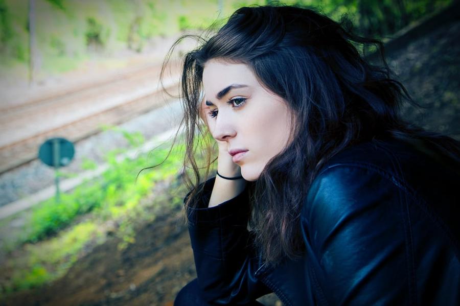A person in a leather jacket and long, dark hair looks off into the distance seriously.