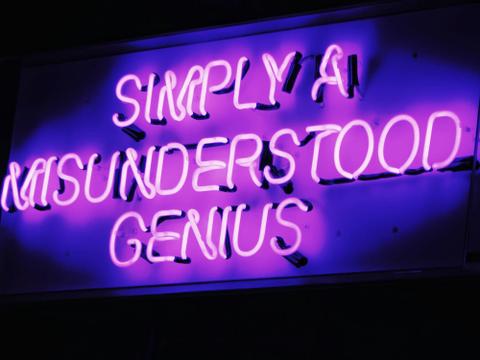 A neon purple sign reads "Simply a misunderstood genius."