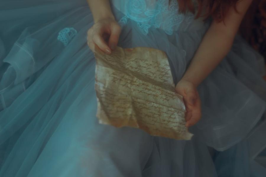 Hands hold a wrinkled sheet of brown paper with an unreadable message on it.