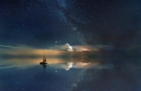 A sailboat sailing on the reflection of a cloudy sunset.
