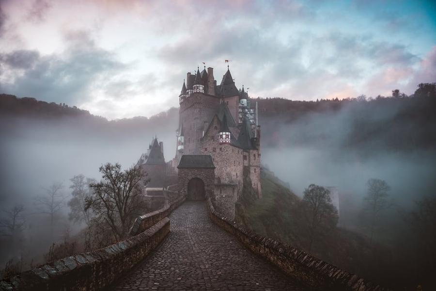 Stone bridge leading to a small castle with mist hanging in the air.