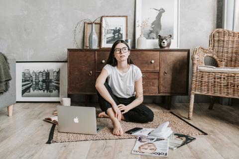A writer sits on the floor with a laptop and a stack of magazines.