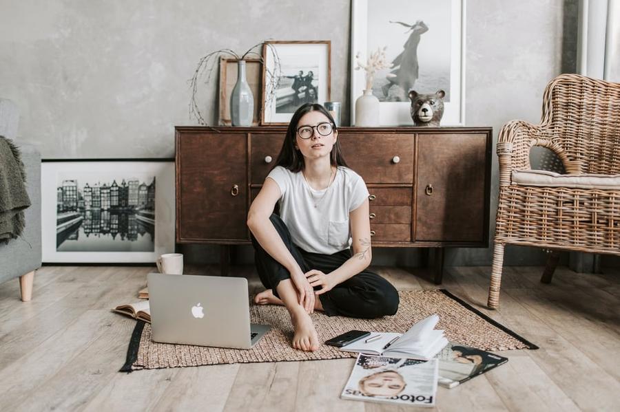 A writer sits on the floor with a laptop and a stack of magazines.