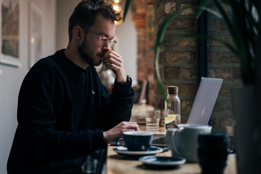 Man thinking in front of a laptop at a cafe.