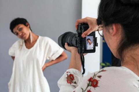 Over-the-shoulder view of a photographer in a white blouse taking a photo of another person posing.