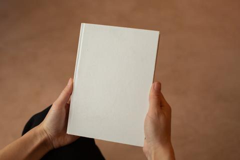 Two hands hold a book with a blank white cover.