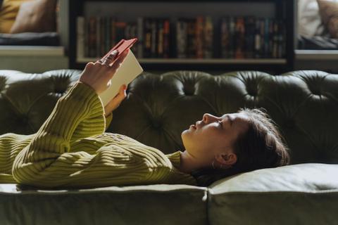 A female-presenting person lies on the floor on their back, reading a sad story.