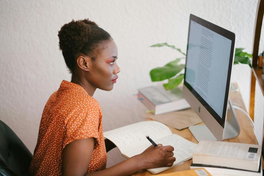 A sensitivity reader sits in front of a computer making notes in a notebook as they read a manuscript on the screen.