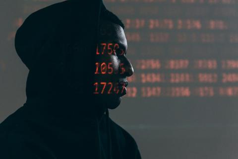 Silhouette of a person in a dark room with computer code projected onto their face.