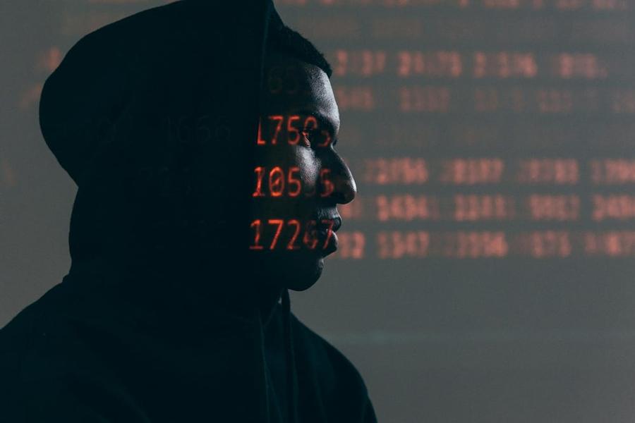 Silhouette of a person in a dark room with computer code projected onto their face.