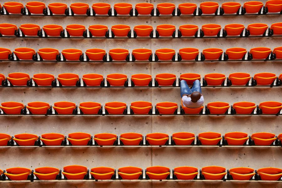 Overhead view of rows of orange stadium chairs with a man sitting in one.