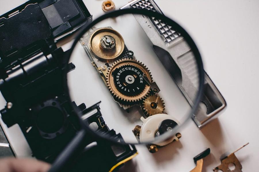 A magnifying glass being held up over watch parts.