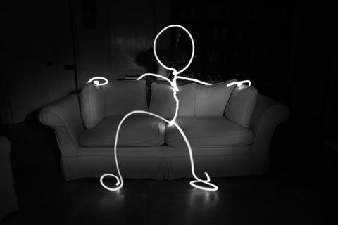 A stick figure made of white neon light reclines on a sofa.