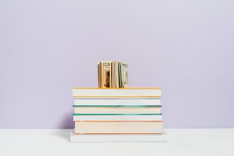 Money rolled up on top of a stack of books.
