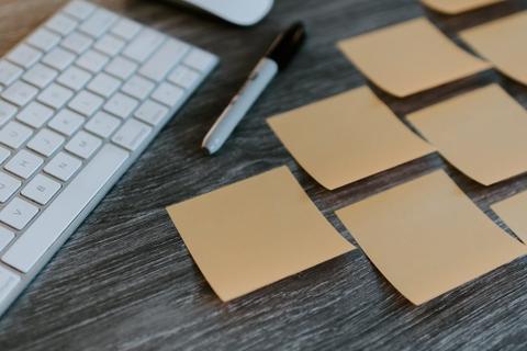 A keyboard, marker, and brown sticky notes on a desk.