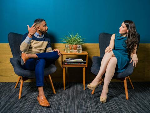 Two well-dressed people sit in chairs and have a conversation.