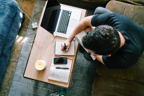 Overhead image of a person sitting at a computer and writing in a notebook.