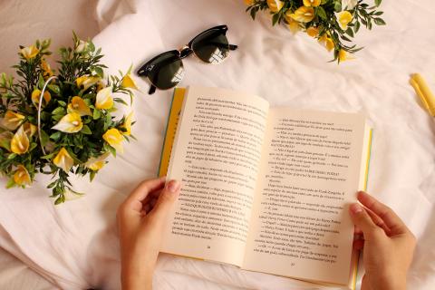 Hands hold a book open on a table with flowers on it.