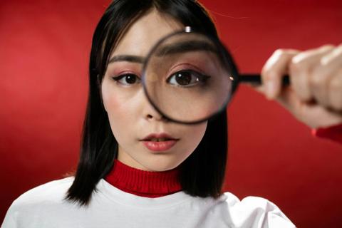 A person holds a magnifying glass up to their eye, making their eye look huge.