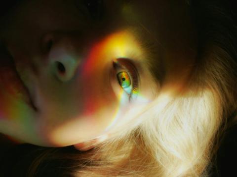 Intense close-up of a bright light shining on a green eye, the face otherwise obscured in darkness.