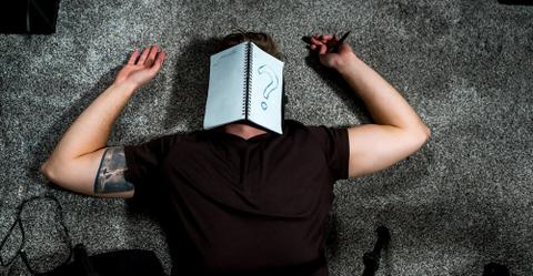 A person lying on their back with an open notebook on their face.