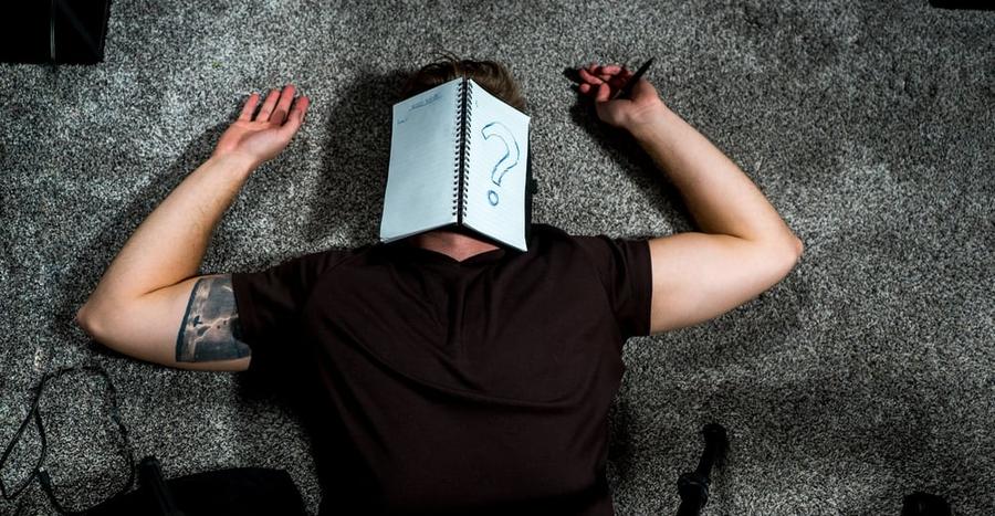A person lying on their back with an open notebook on their face.
