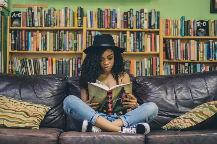 Woman reading while sitting cross-legged on a couch in front of a bookshelf.