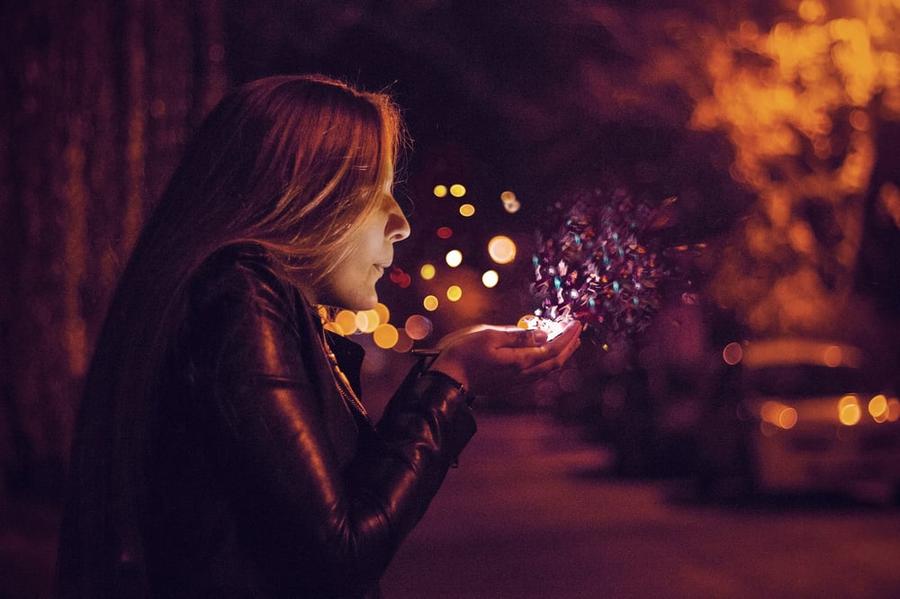 A woman blowing into her cupped hands, magical glitter floating outwards.
