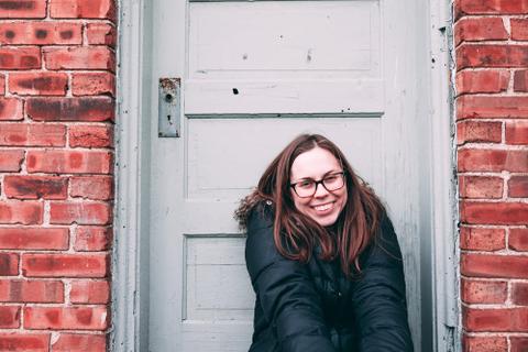A person in a coat smiles in front of a door.