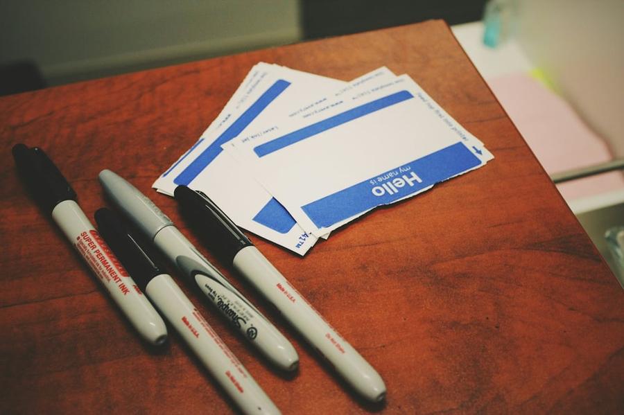 Four markers on wooden table next to a pile of name tag stickers.