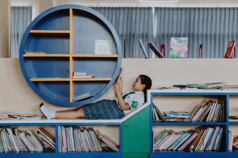 A child lies across a bookshelf, reading middle grade fiction. 